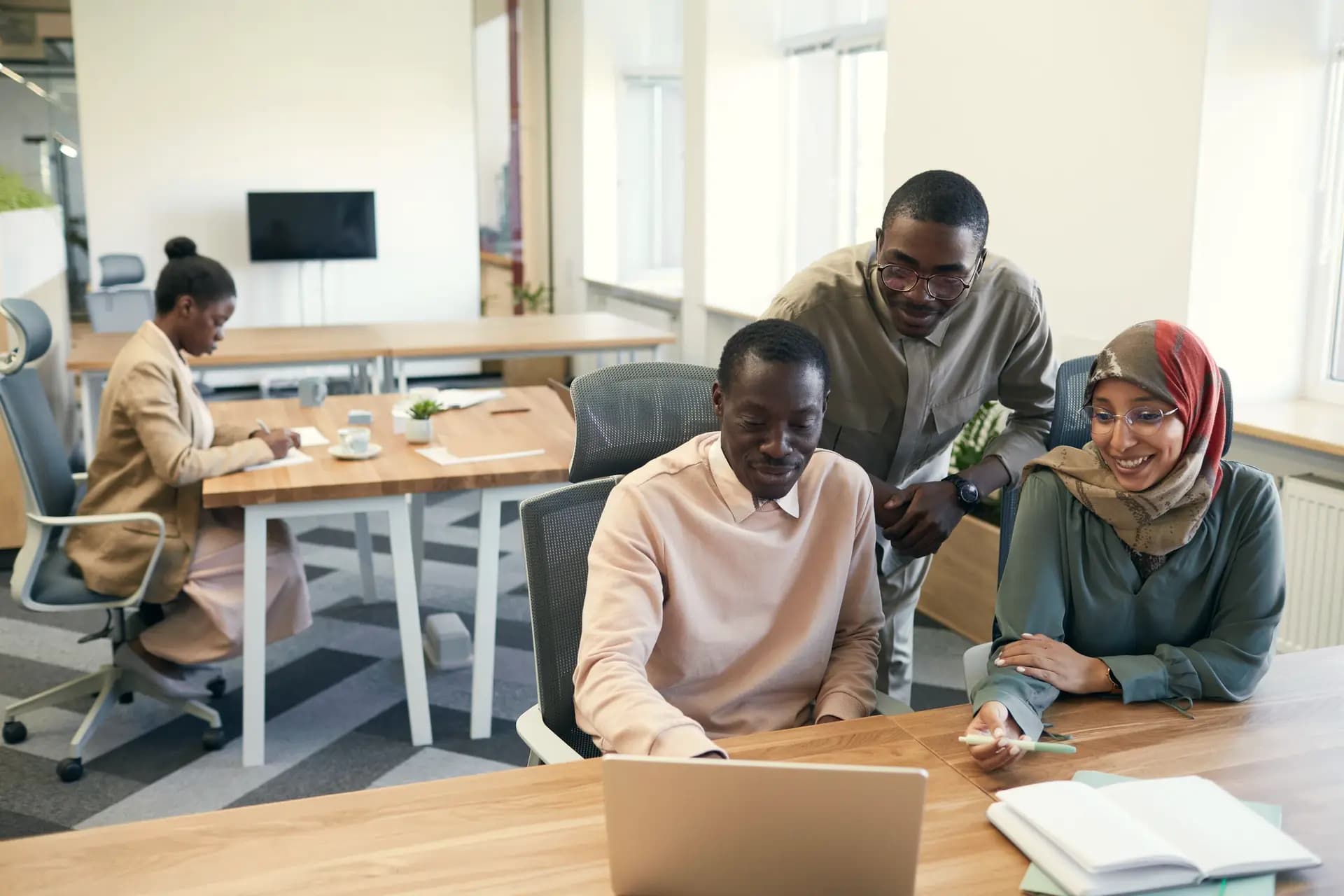 Colleagues gather around a laptop in a shared office.