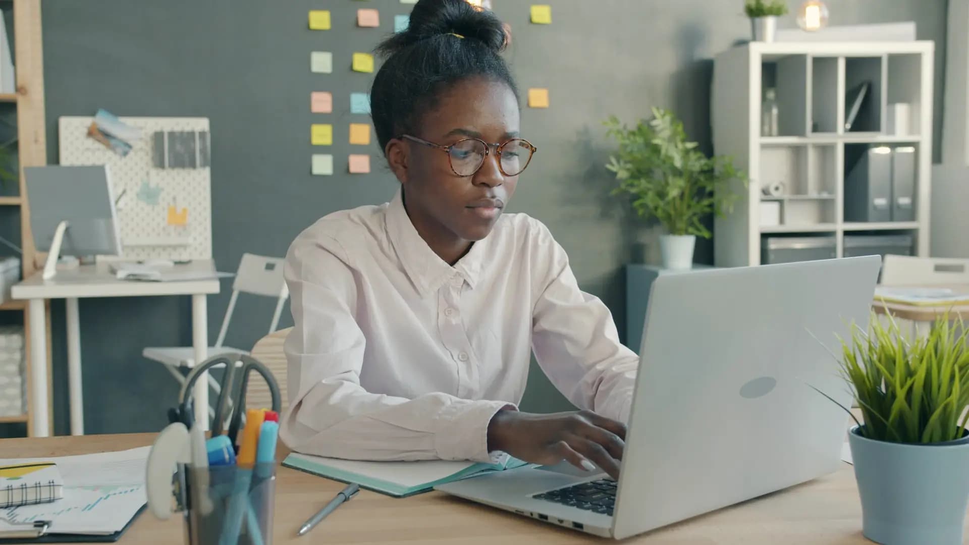 A woman works on her laptop at a bright desk.