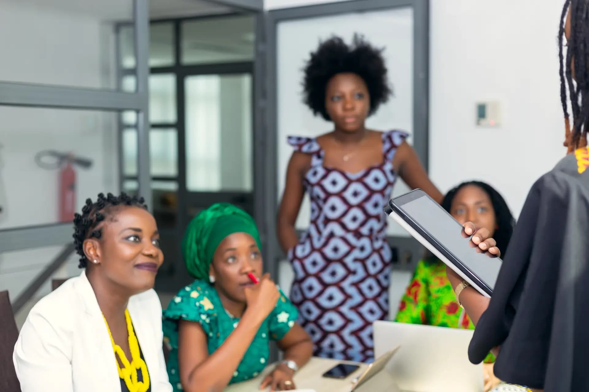 A team of women review work together around a tablet and a laptop.