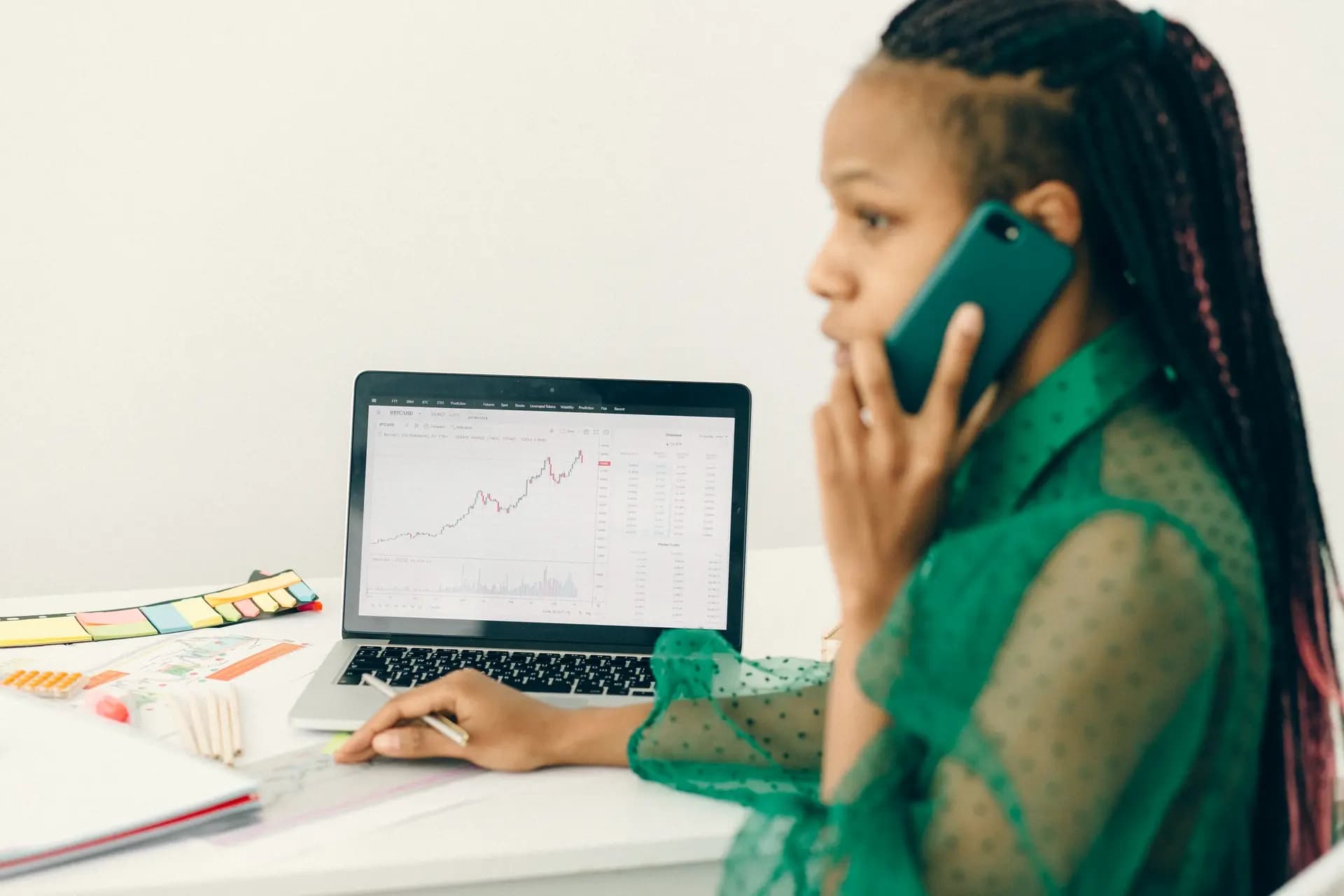 A woman takes a phone call while she reviews a chart on her laptop.